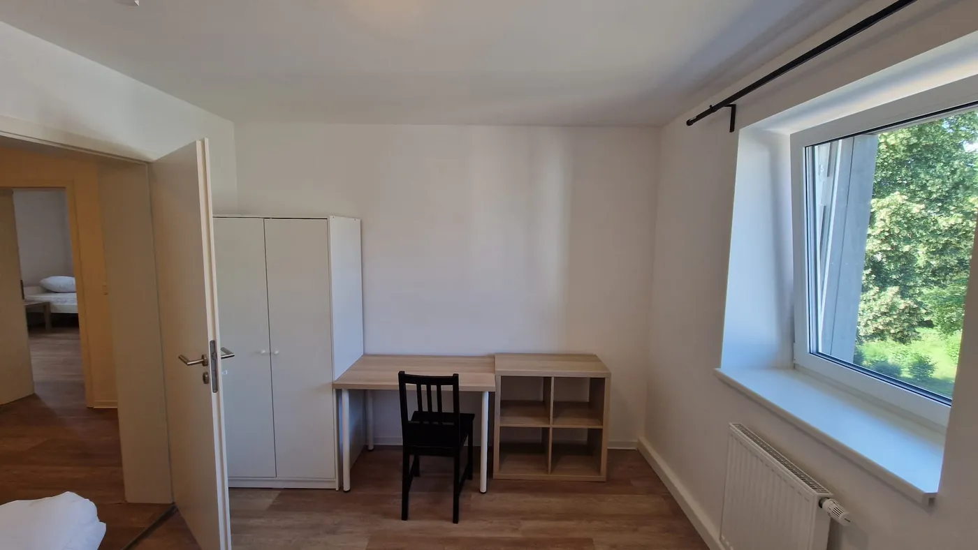 Renoviertes Zimmer der Monteurunterkunft im Raum Landshut mit Einzelbett, Schreibtisch und Kleiderschrank am großen Fenster