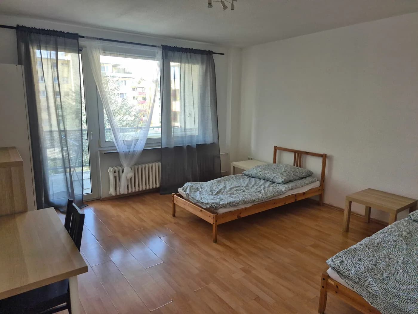 Helles Zimmer einer Monteurwohnung in Neu-Isenburg mit getrennten Einzelbetten, Esstisch und Balkonzugang auf Laminatboden