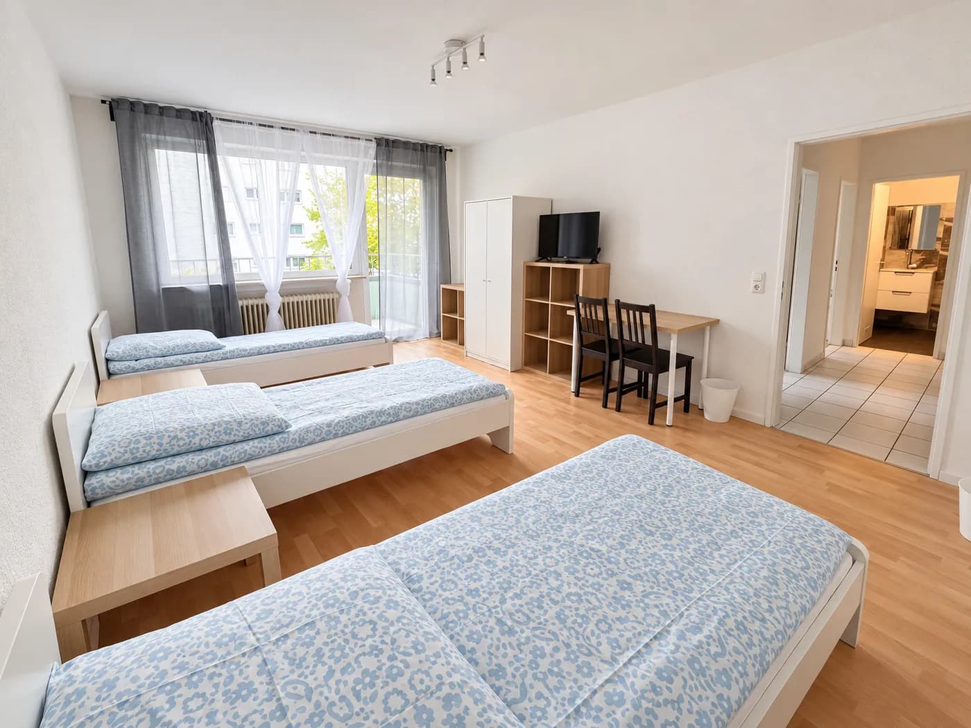 Helles Zimmer mit drei sichtbaren Einzelbetten in einer Wohnung