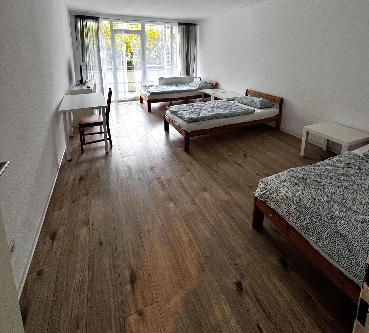 Geräumiges Zimmer der Monteurunterkunft im Raum Aachen mit mehreren getrennten Einzelbetten, Schreibtisch und Balkontür
