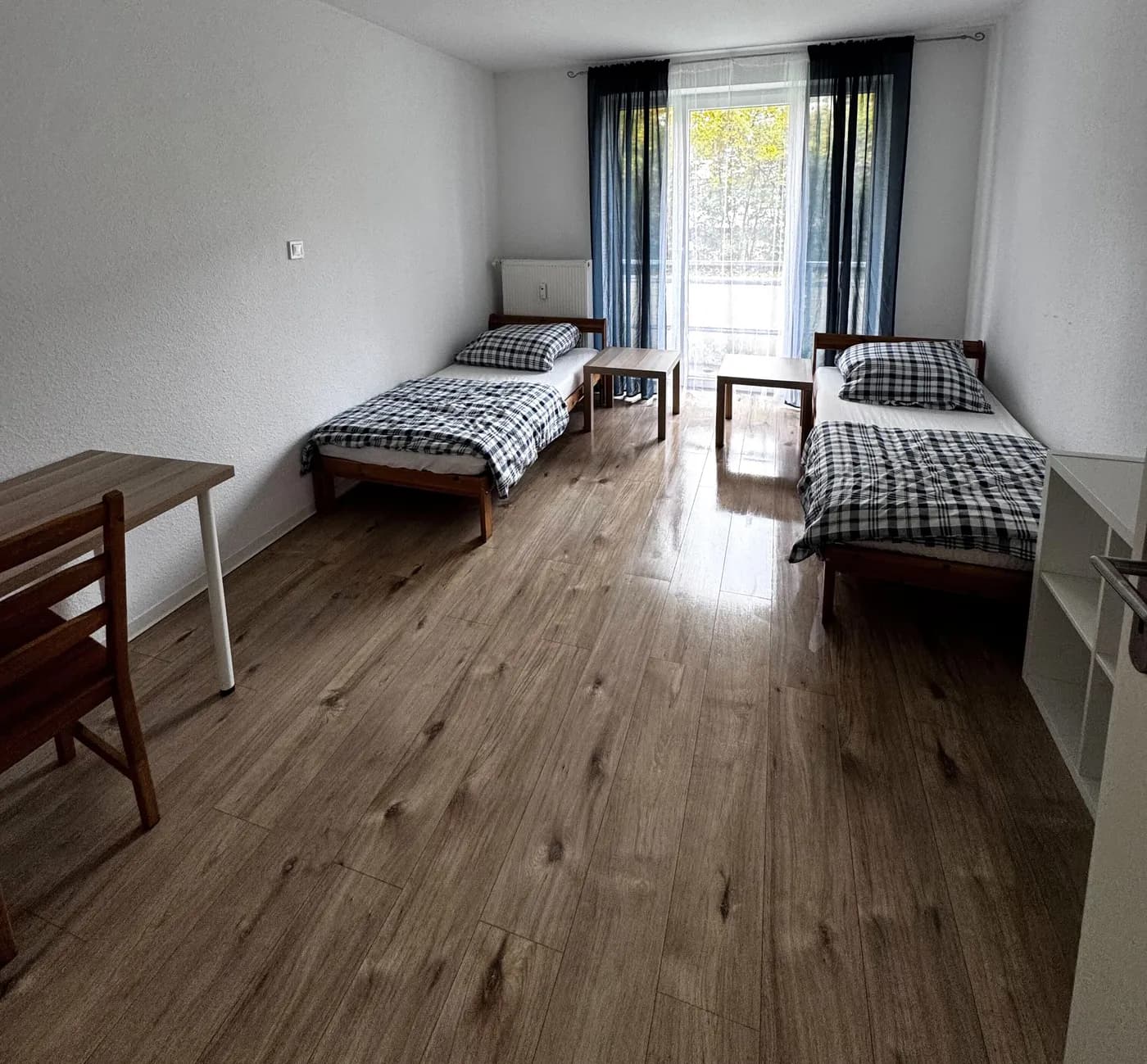 Helles Schlafzimmer einer Monteurwohnung im Raum Aachen mit zwei getrennten Einzelbetten und Arbeitstisch auf hellem Holzboden