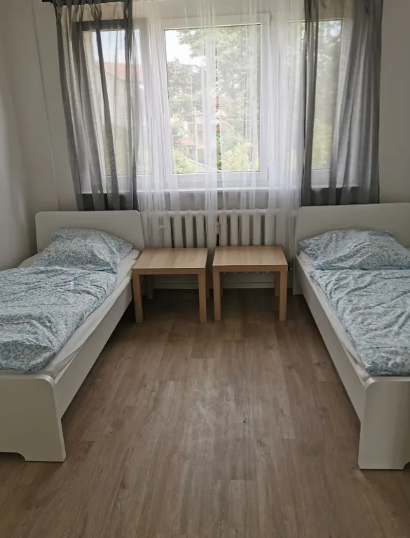 Helles Schlafzimmer einer Monteurwohnung in Borsdorf mit zwei getrennten Einzelbetten, Nachttischen und Fenster auf modernem Laminatboden