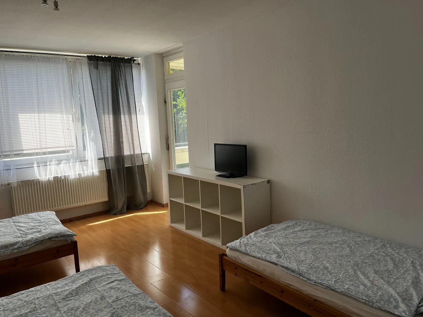 Helles Zimmer einer Monteurwohnung in Erkrath mit zwei getrennten Einzelbetten, Regal und Fernseher auf Laminatboden