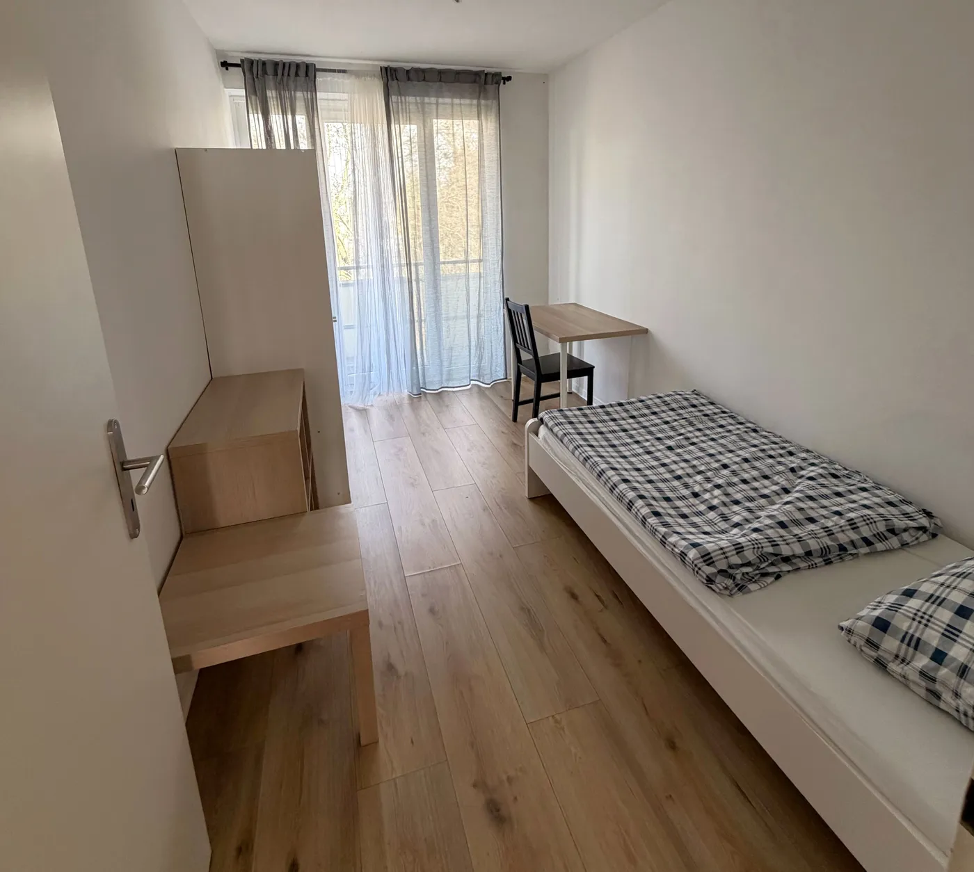 Helles Monteurzimmer in Eschweiler mit Einzelbett, Schreibtisch und Balkontür auf hellem Holzboden