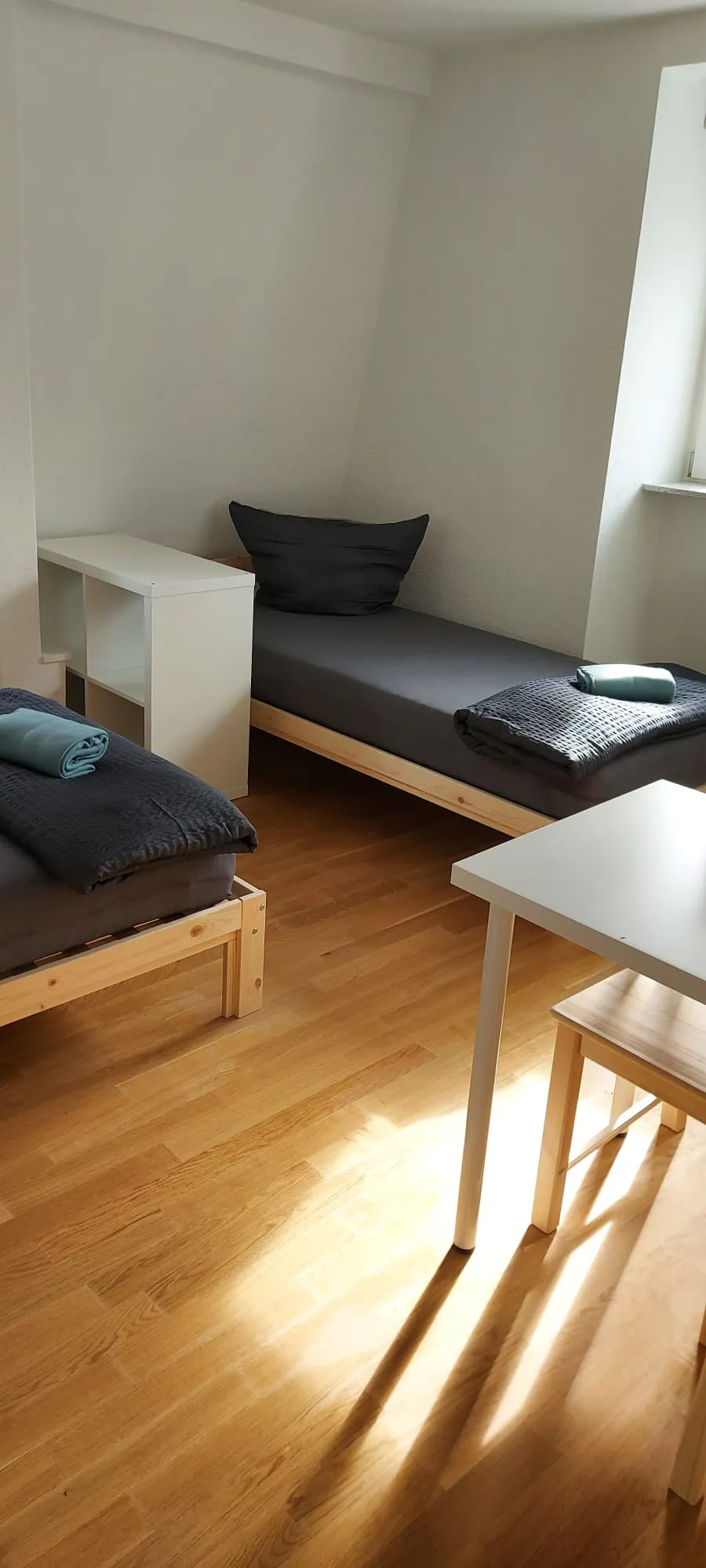 Weiteres sonniges Zimmer der Monteurunterkunft in Friedrichshafen mit zwei Einzelbetten, Regal und Esstisch auf Eichenparkett