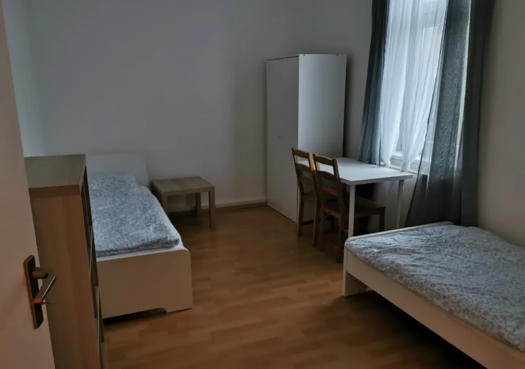 Helles Schlafzimmer einer Monteurwohnung in Heidenau mit zwei getrennten Einzelbetten, Esstisch und Kleiderschrank auf Laminatboden