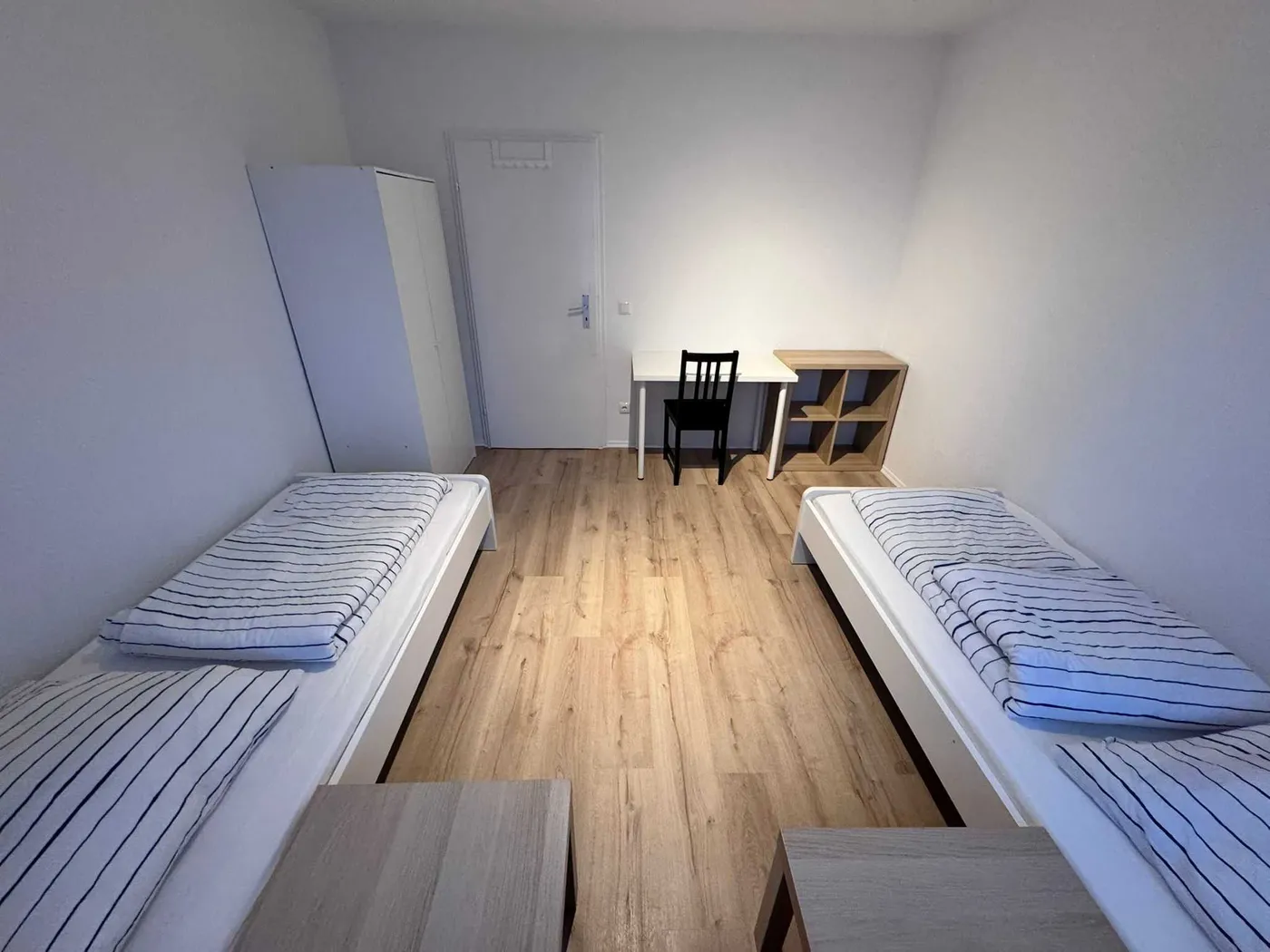 Helles Schlafzimmer einer Monteurwohnung in Hürth mit zwei getrennten Einzelbetten, Schreibtisch und Kleiderschrank auf Laminatboden