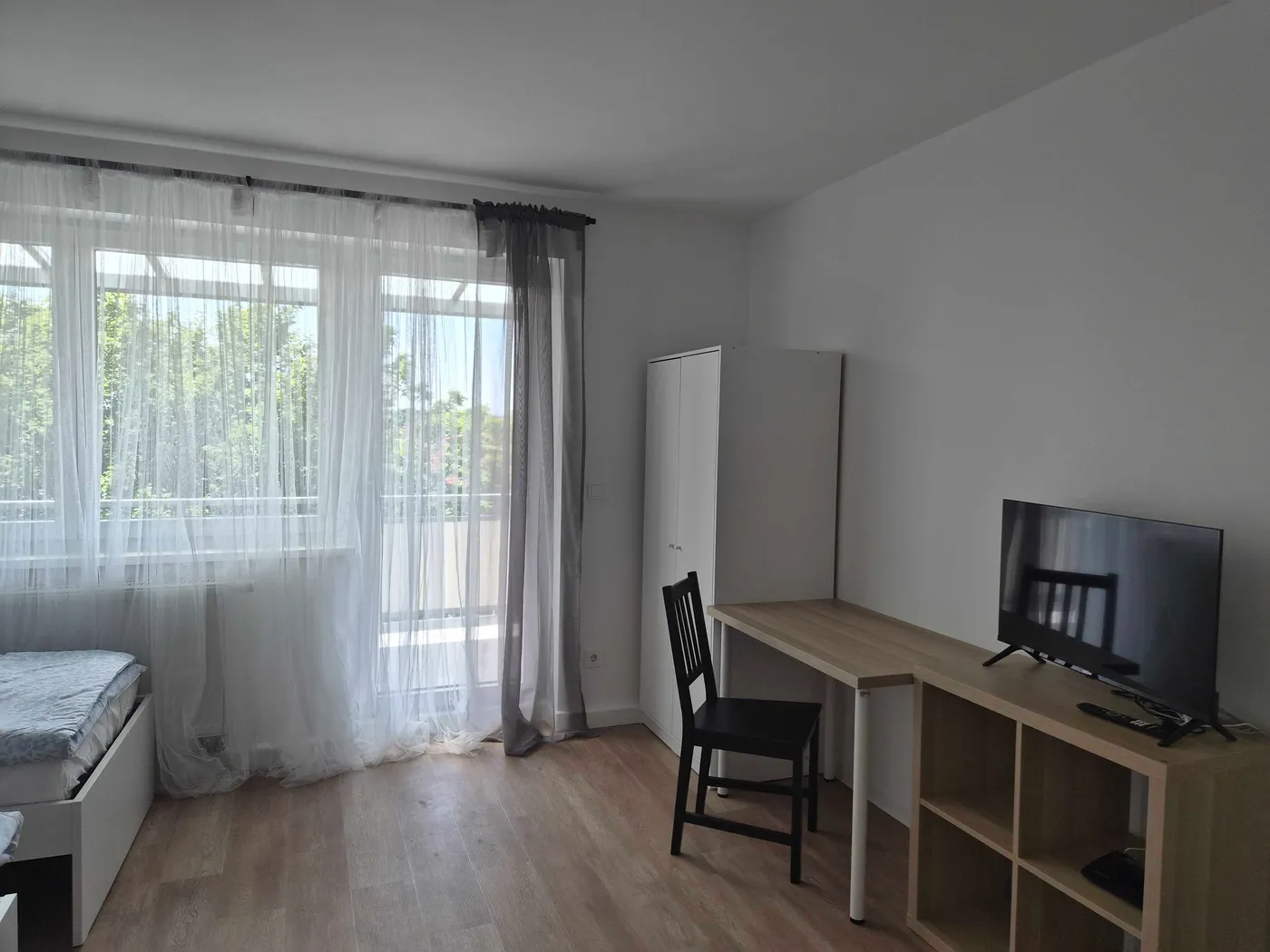 Zimmer mit Schreibtisch, Fernseher und Balkontür in derselben Wohnung in Kösching