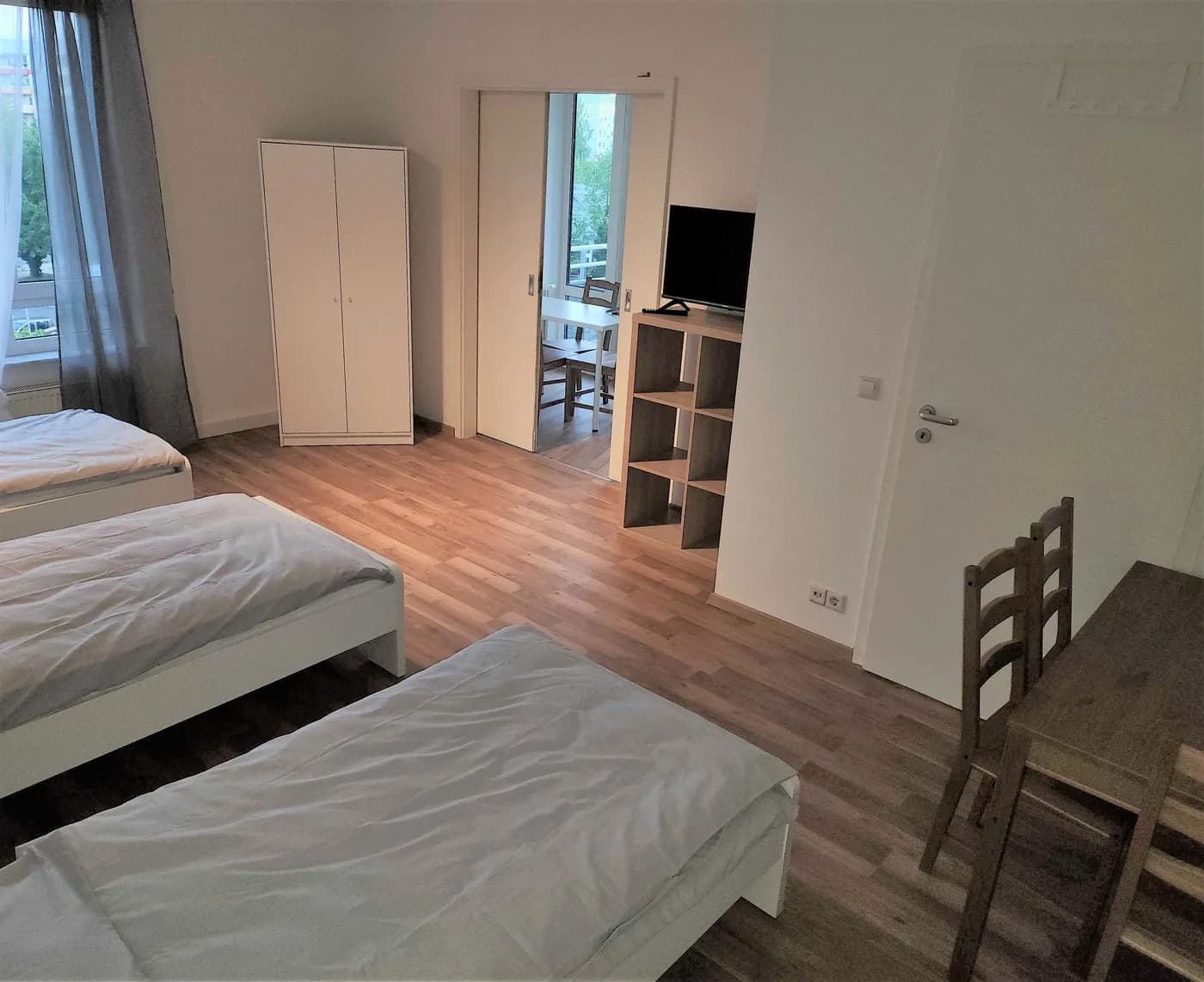 Helles Zimmer einer Monteurwohnung in Leipzig mit zwei getrennten Einzelbetten, Kleiderschrank, Fernseher und Esstisch auf Laminatboden