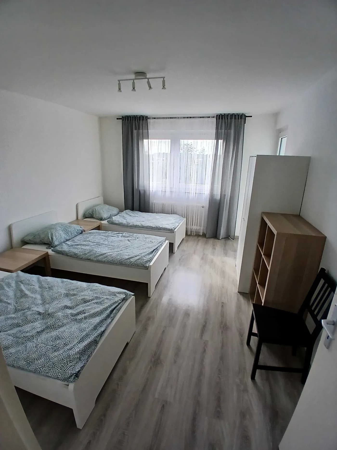 Geräumiges Schlafzimmer einer Monteurunterkunft mit drei Einzelbetten und großem Fenster