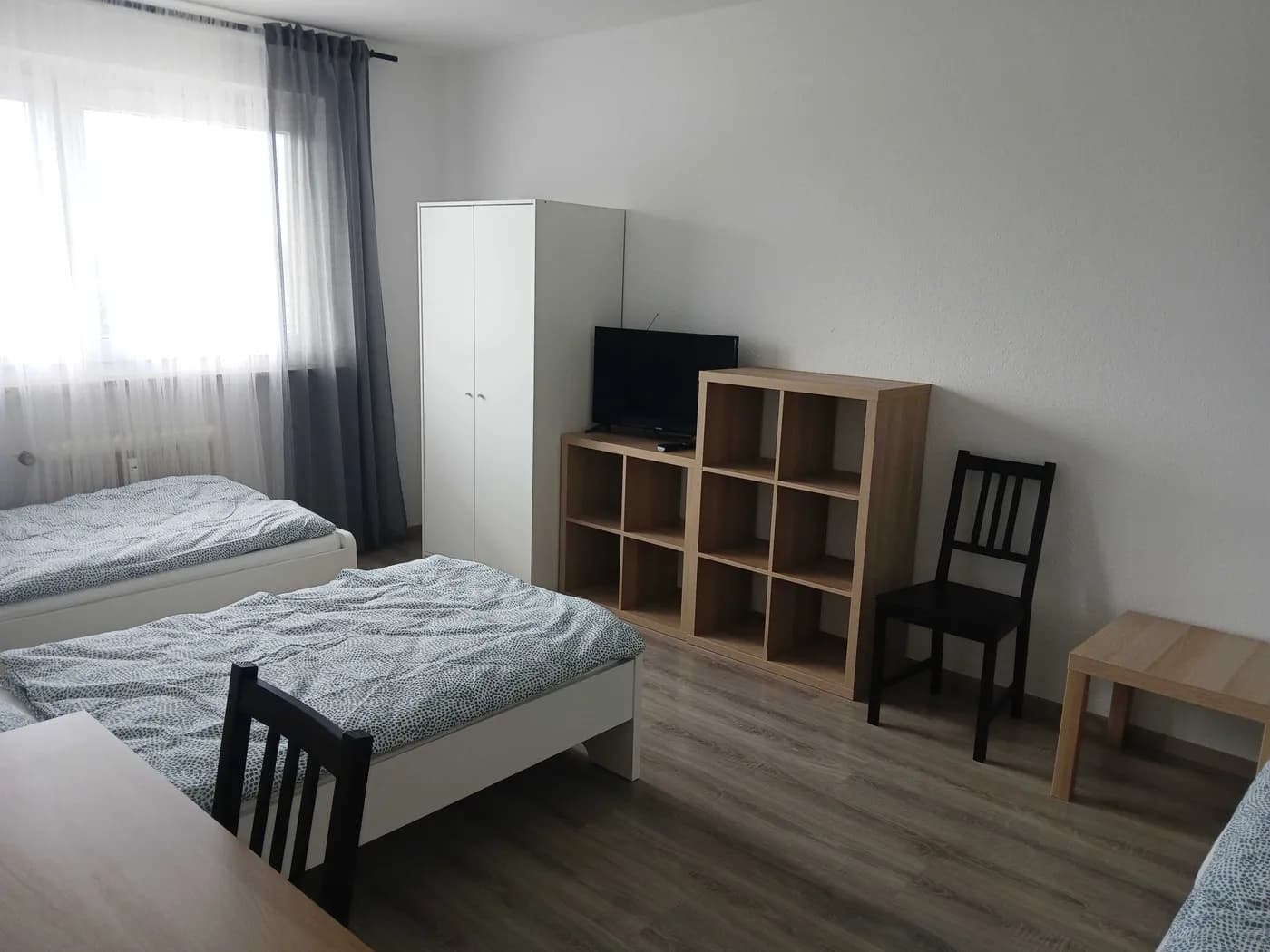Helles Schlafzimmer einer Monteurwohnung mit zwei Einzelbetten, TV und offenem Regal