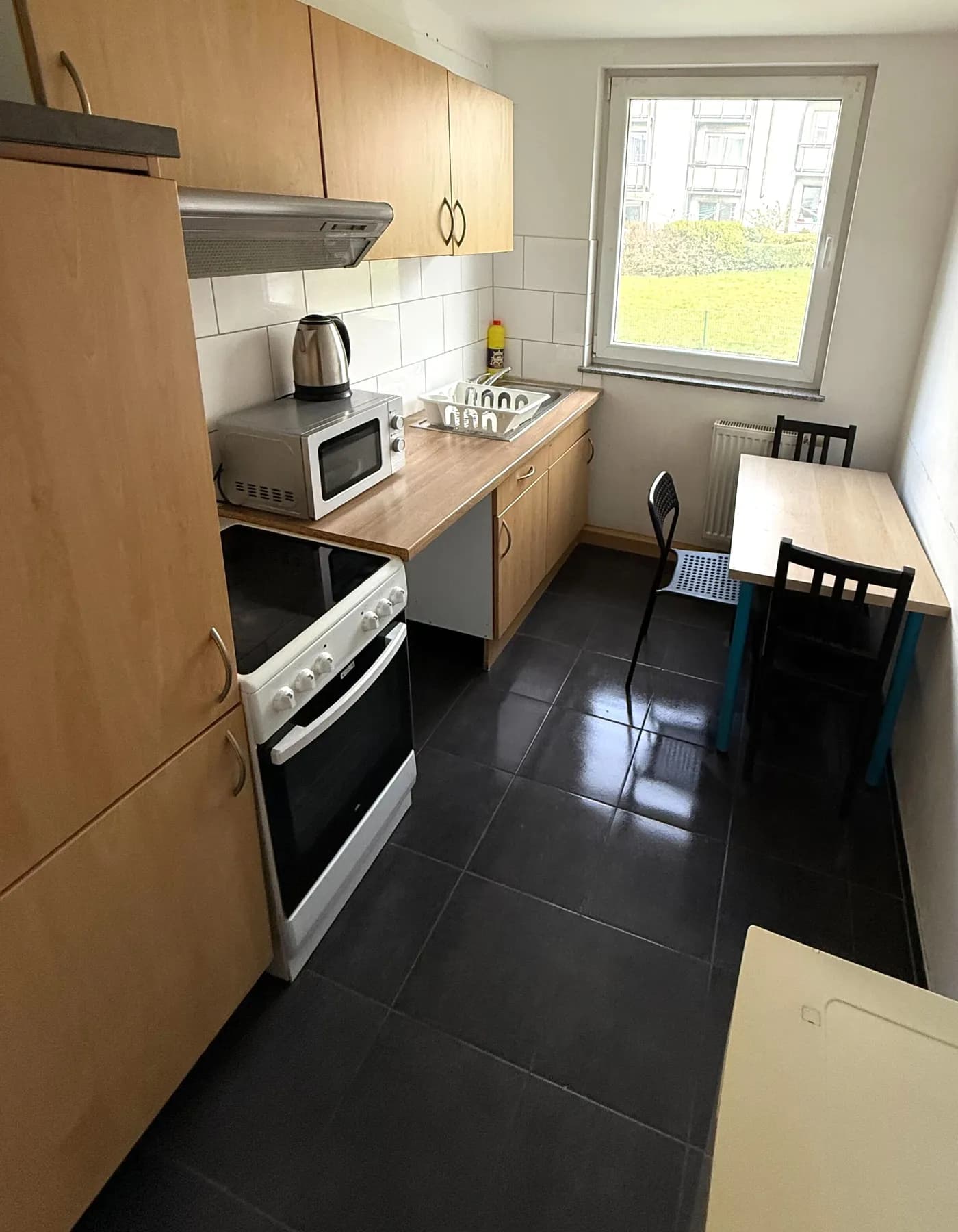 Voll ausgestattete Küche mit Herd, Backofen, Mikrowelle und Esstisch am Fenster in einer Monteurwohnung in Remscheid