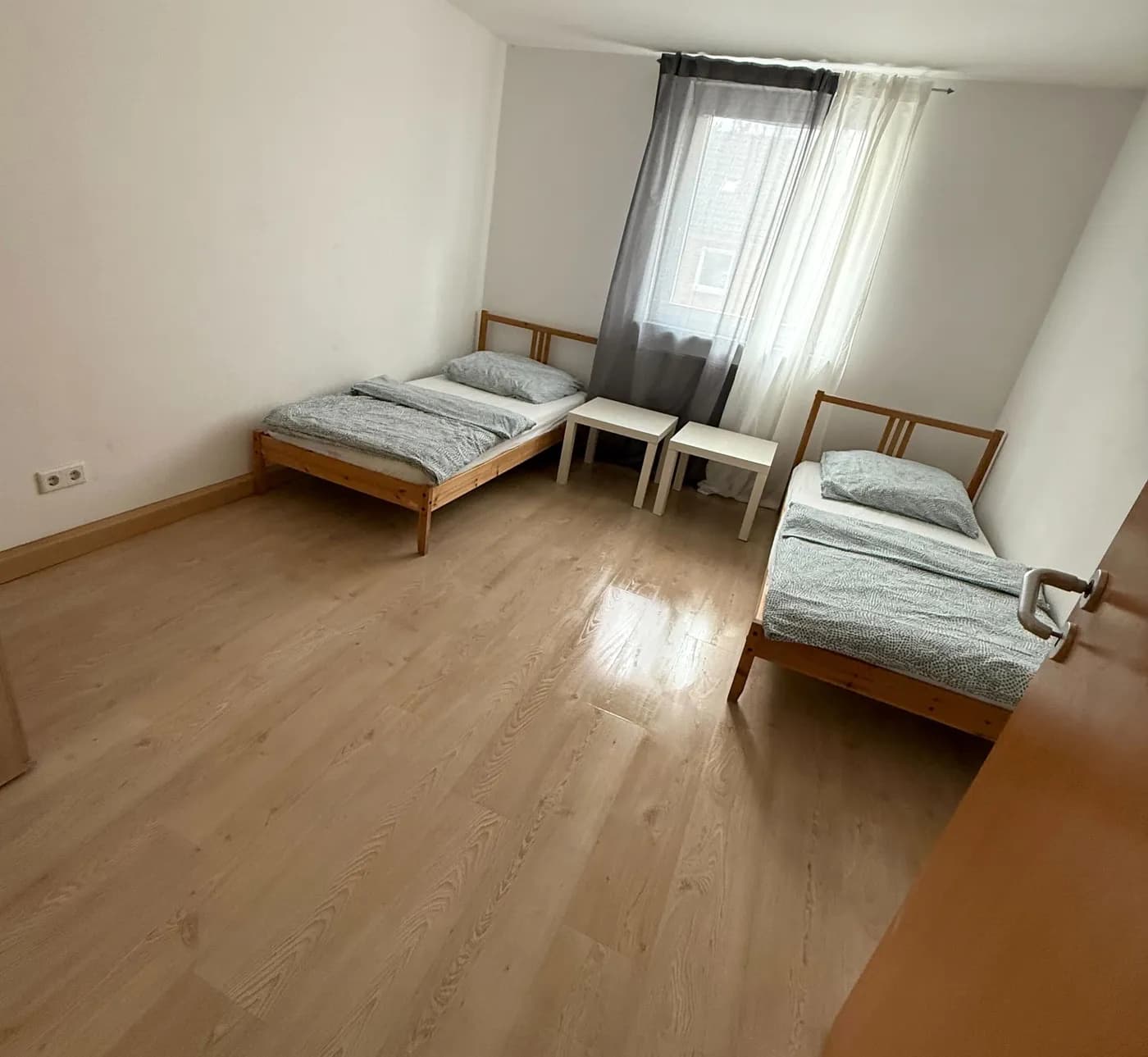 Helles Zimmer einer Monteurwohnung in Remscheid mit zwei getrennten Einzelbetten, Nachttischen und großem Fenster